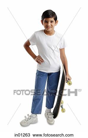 Stock Image - Boy standing, holding skateboard, hand on hip. Fotosearch