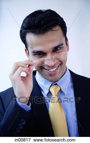 Stock Photo -  Businessman adjusting glasses, smiling at camera. Fotosearch