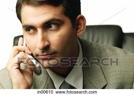 Stock Image - Businessman holding mobile phone, looking away. Fotosearch