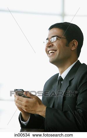 Businessman holding PDA, smiling, looking away View Large Photo Image Picture - Businessman holding PDA, smiling, looking away. Fotosearch