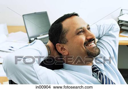 Businessman in office, hands behind head View Large Photo Image Picture - Businessman in office, hands behind head. Fotosearch