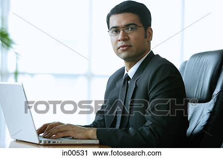 Businessman in office, sitting at desk, looking at camera View Large Photo Image Stock Image - Businessman in office, sitting at desk, looking at camera. Fotosearch