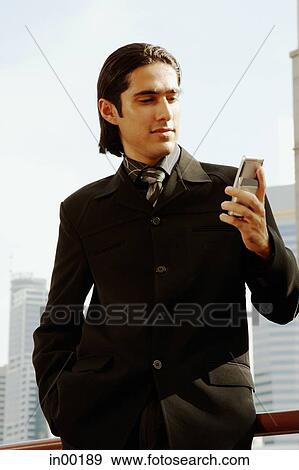 Stock Photo - Businessman looking at mobile phone, hands in pocket. Fotosearch