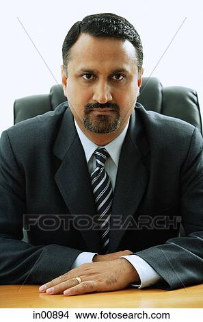 Picture - Businessman sitting at desk, looking at camera. Fotosearch