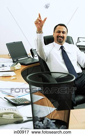Businessman sitting in office throwing paper ball into dustbin, smiling View Large Photo Image Stock Photo - Businessman sitting in office throwing paper ball into dustbin, smiling. Fotosearch
