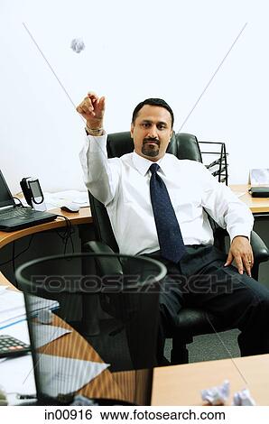 Businessman sitting in office throwing paper ball into dustbin View Large Photo Image Stock Photograph - Businessman sitting in office throwing paper ball into dustbin. Fotosearch