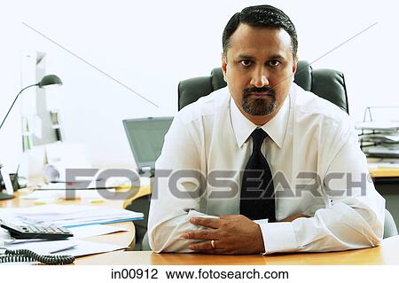 Stock Image - Businessman sitting, looking at camera, portrait. Fotosearch