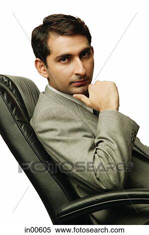 Stock Photography - Businessman sitting on chair, hand on chin, looking at camera. Fotosearch