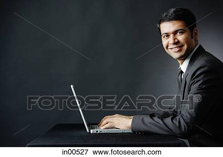 Businessman smiling at camera, using laptop View Large Photo Image Stock Photo - Businessman smiling at camera, using laptop. Fotosearch