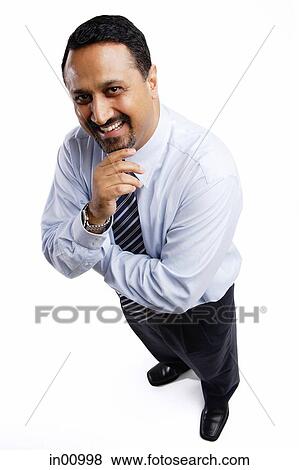 Stock Photo - Businessman smiling up at camera, arms crossed, hand on chin. Fotosearch