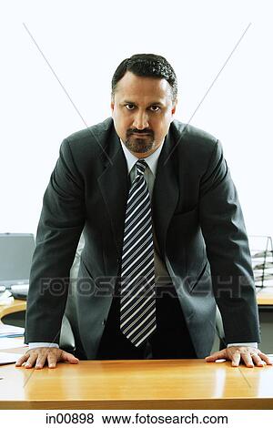 Stock Photo - Businessman standing at desk, looking at camera. Fotosearch
