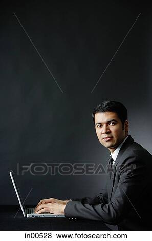 Stock Photo - Businessman using laptop, looking at camera, portrait. Fotosearch