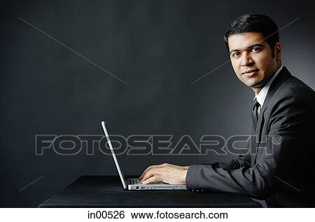 Stock Photograph - Businessman using laptop, looking at camera. Fotosearch