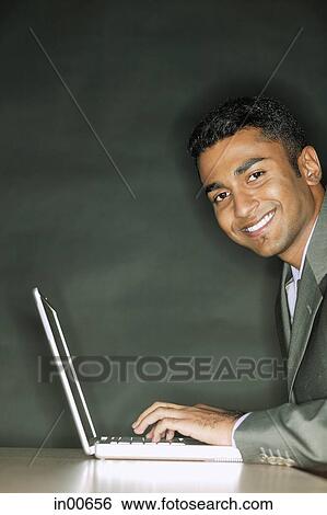 Stock Photograph - Businessman using laptop, smiling at camera. Fotosearch