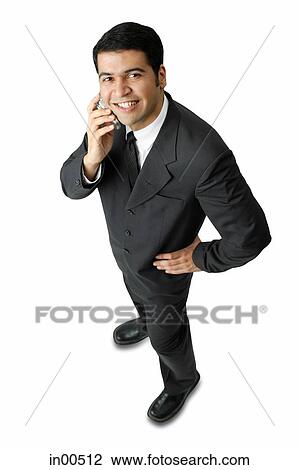 Stock Image - Businessman, using mobile phone, looking at camera, hand on hip. Fotosearch