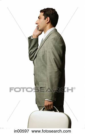 Stock Photo - Businessman using mobile phone, carrying briefcase, side view. Fotosearch