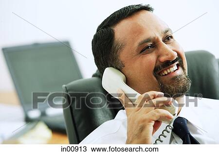 Stock Image - Businessman using telephone, looking away. Fotosearch