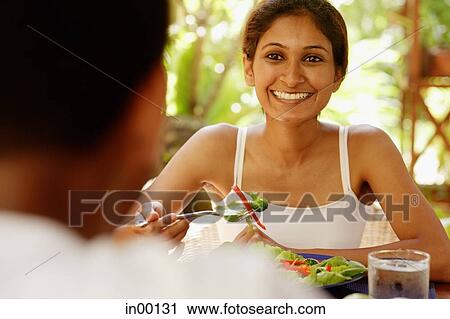 Stock Image - Couple eating, woman holding fork and smiling at man across from her. Fotosearch
