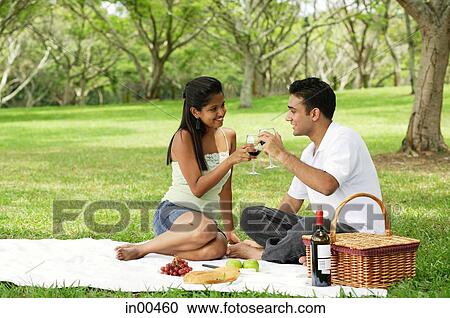 Stock Image - Couple having picnic, toasting with wine glasses. Fotosearch