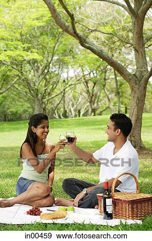 Couple in park, having a picnic, toasting with wine glasses View Large Photo Image Stock Photo - Couple in park, having a picnic, toasting with wine glasses. Fotosearch