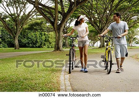 Couple in park, holding bicycles, walking View Large Photo Image Picture - Couple in park, holding bicycles, walking. Fotosearch