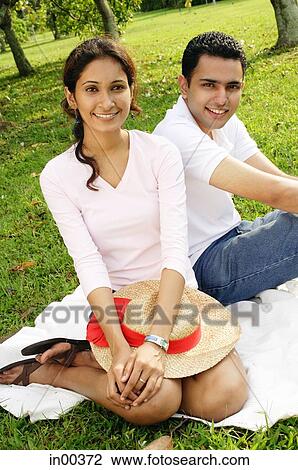 Couple in park, sitting on grass, looking at camera View Large Photo Image Stock Image - Couple in park, sitting on grass, looking at camera. Fotosearch