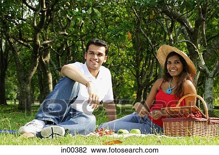 Couple in park, sitting on grass, having picnic, looking at camera View Large Photo Image Stock Image - Couple in park, sitting on grass, having picnic, looking at camera. Fotosearch