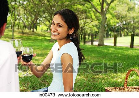 Stock Image - Couple in park, toasting with wine glasses. Fotosearch