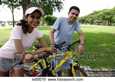 Stock Photo - Couple leaning on bicycles, looking at camera. Fotosearch