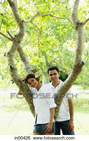 Stock Photograph - Couple looking at camera, tree between them. Fotosearch