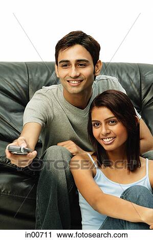 Stock Image - Couple sitting and facing forward, man holding remote control. Fotosearch