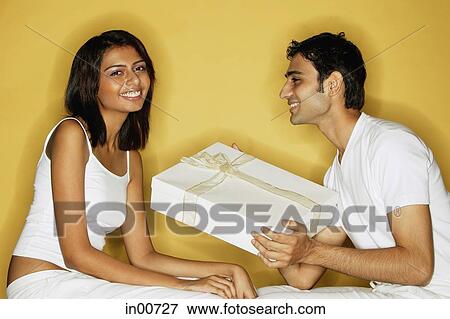 Stock Photo - Couple sitting face to face, woman looking at camera, man holding gift. Fotosearch
