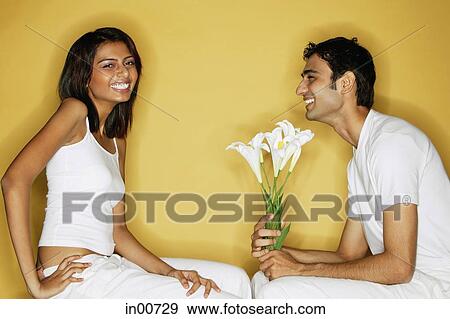 Couple sitting face to face, woman looking at camera, man holding bouquet of flowers View Large Photo Image Stock Photo - Couple sitting face to face, woman looking at camera, man holding bouquet of flowers. Fotosearch