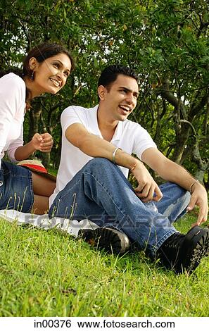 Couple sitting on grass, looking away View Large Photo Image Stock Photograph - Couple sitting on grass, looking away. Fotosearch