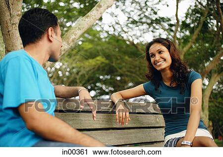Couple sitting on park bench, talking View Large Photo Image Stock Image - Couple sitting on park bench, talking. Fotosearch