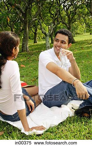 Couple sitting on picnic blanket, facing each other, man drinking from water bottle View Large Photo Image Stock Photography - Couple sitting on picnic blanket, facing each other, man drinking from water bottle. Fotosearch