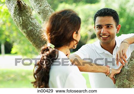 Couple smiling at each other, standing on either side of tree View Large Photo Image Stock Photo - Couple smiling at each other, standing on either side of tree. Fotosearch