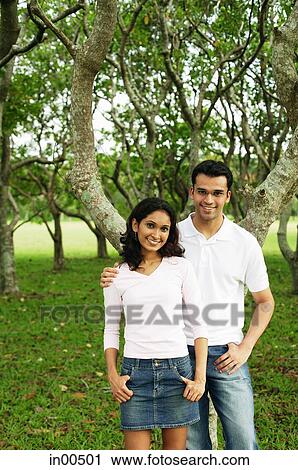 Stock Image - Couple standing in park, looking at camera. Fotosearch