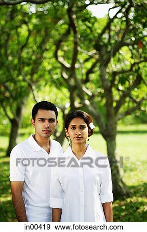 Couple standing in park, looking at camera View Large Photo Image Stock Photo - Couple standing in park, looking at camera. Fotosearch
