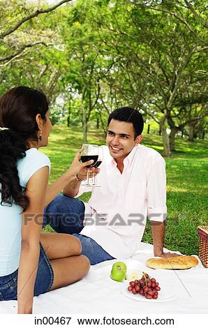 Stock Photo - Couple toasting with wine glasses, sitting on picnic blanket. Fotosearch