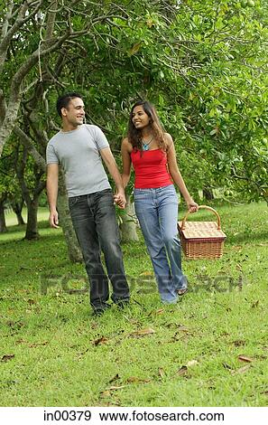 Couple walking in park, holding hands, woman carrying picnic basket View Large Photo Image Stock Photo - Couple walking in park, holding hands, woman carrying picnic basket. Fotosearch