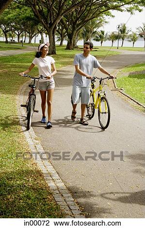 Couple wheeling bicycles in park View Large Photo Image Stock Image - Couple wheeling bicycles in park. Fotosearch