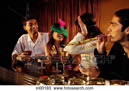 Stock Image - Couples at bar, having fun with noisemakers and mask. Fotosearch