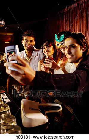Stock Image - Couples at bar, taking picture with mobile phone camera. Fotosearch