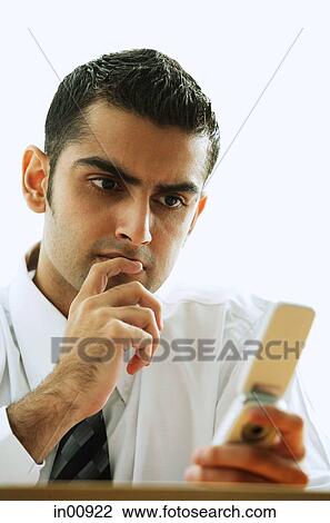 Stock Image - Executive looking at mobile phone, hand on chin. Fotosearch