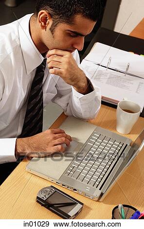 Executive sitting at desk, using laptop View Large Photo Image Stock Photo - Executive sitting at desk, using laptop. Fotosearch