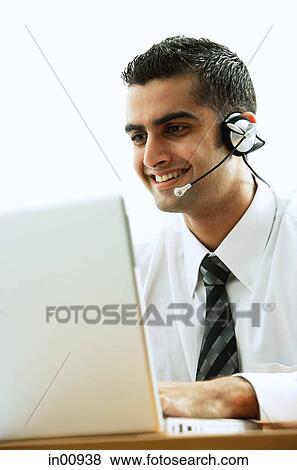 Executive using headset, smiling, using laptop View Large Photo Image Stock Photo - Executive using headset, smiling, using laptop. Fotosearch