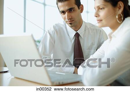 Executives sitting side by side, looking at laptop View Large Photo Image Stock Image - Executives sitting side by side, looking at laptop. Fotosearch