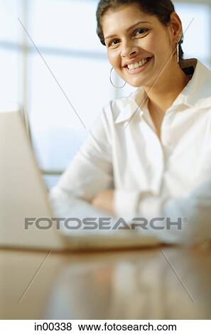 Female executive in front of laptop, smiling at camera View Large Photo Image Stock Photo - Female executive in front of laptop, smiling at camera. Fotosearch