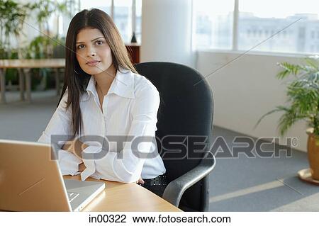 Stock Image - Female executive sitting in office, looking at camera, portrait. Fotosearch